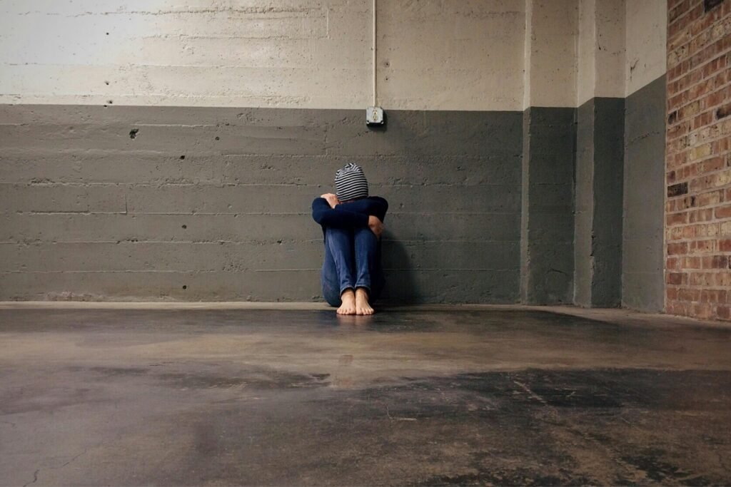 Person sitting in an empty room against a concrete wall, conveying solitude and despair.